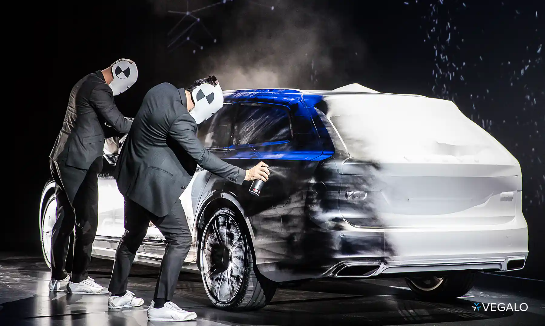 event photo of two men on stage, dressed in costume and spray painting a car