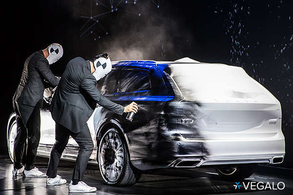 two men on stage, wearing masks and spray painting a car during